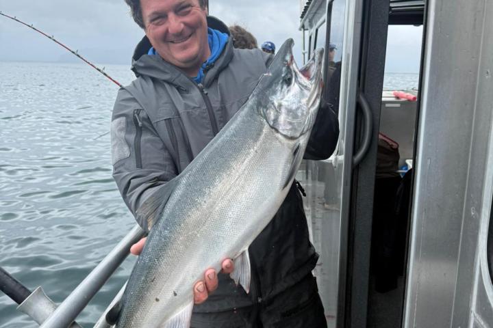 Person holding a large fish on a boat, with a cloudy sky in the background.