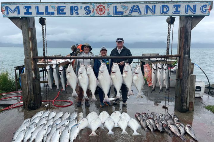 Three people stand by a sign labeled 'Miller's Landing' with numerous large fish hanging and lying beneath.