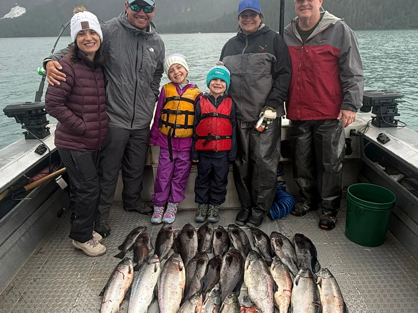Group of people on a boat with a large catch of fish displayed on the deck.