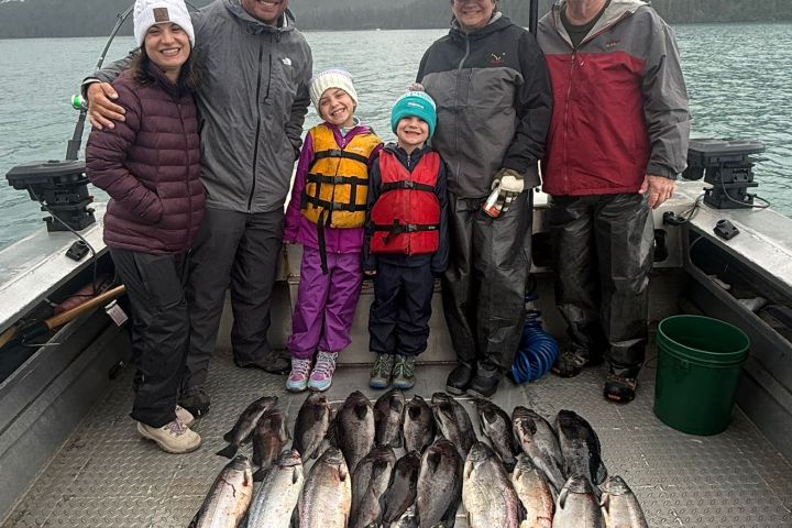 Group of people on a boat with a large catch of fish displayed on the deck.