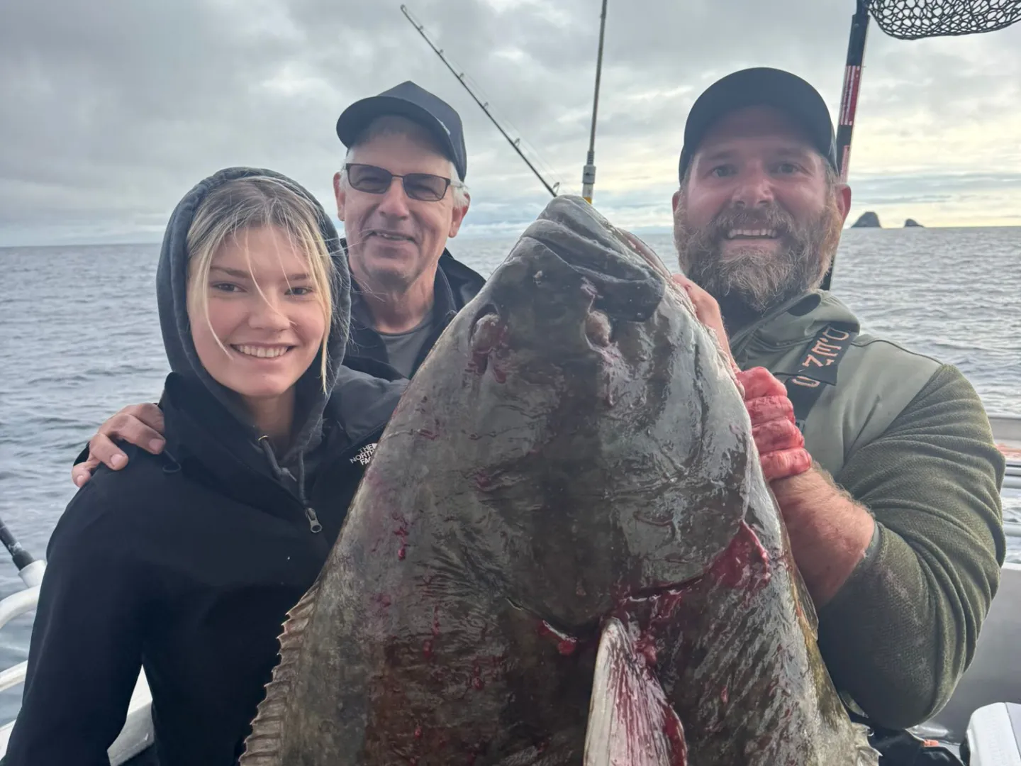 Three people on a boat holding a large fish, with fishing rods in the background.