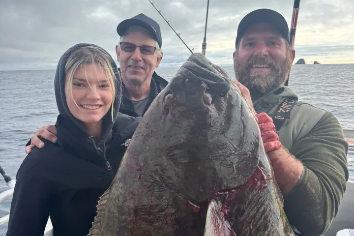 Three people on a boat holding a large fish, with fishing rods in the background.