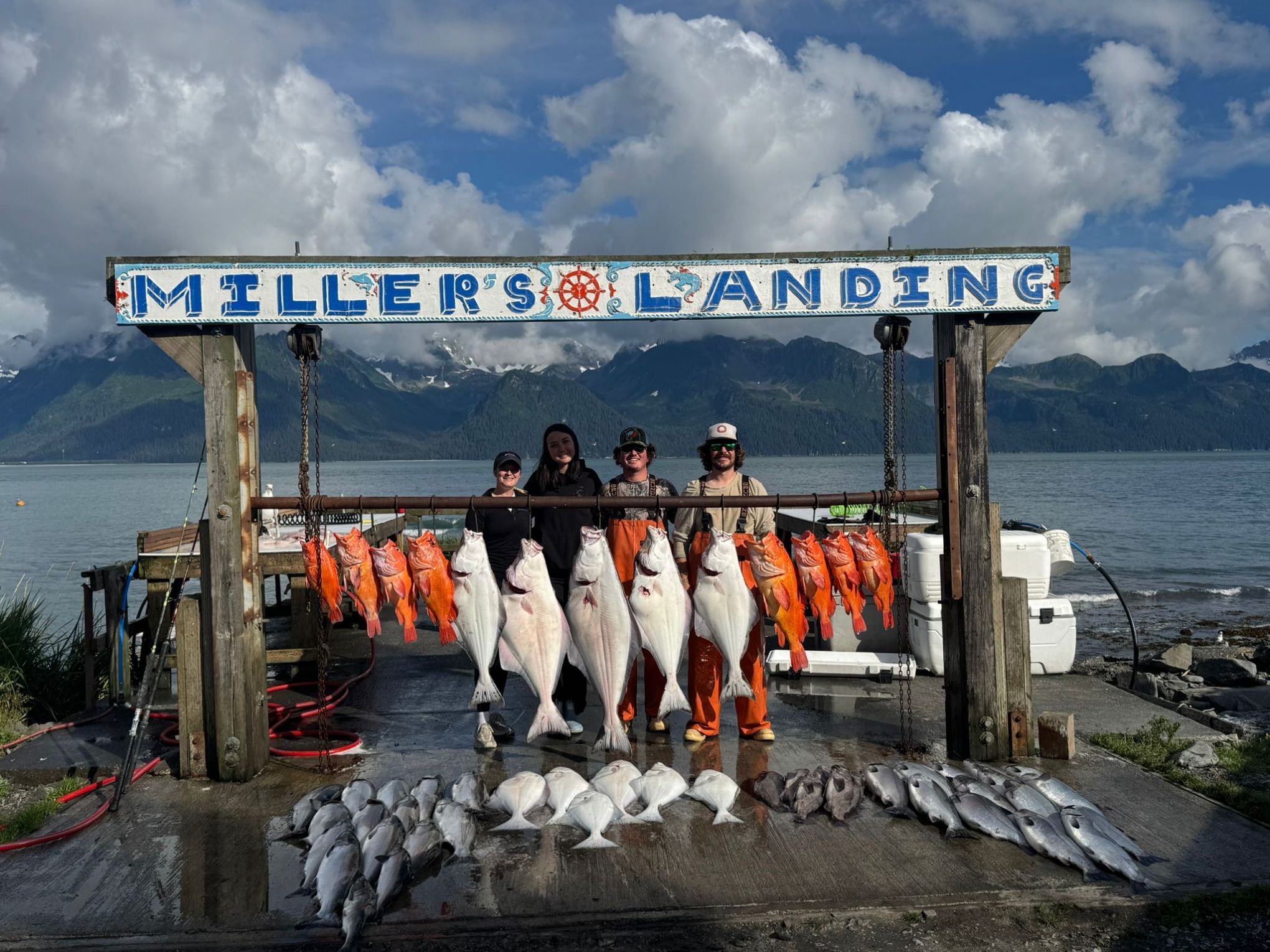 Four people posing with large fish catch at Miller's Landing with mountains in the background.
