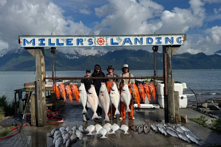 Four people posing with large fish catch at Miller's Landing with mountains in the background.