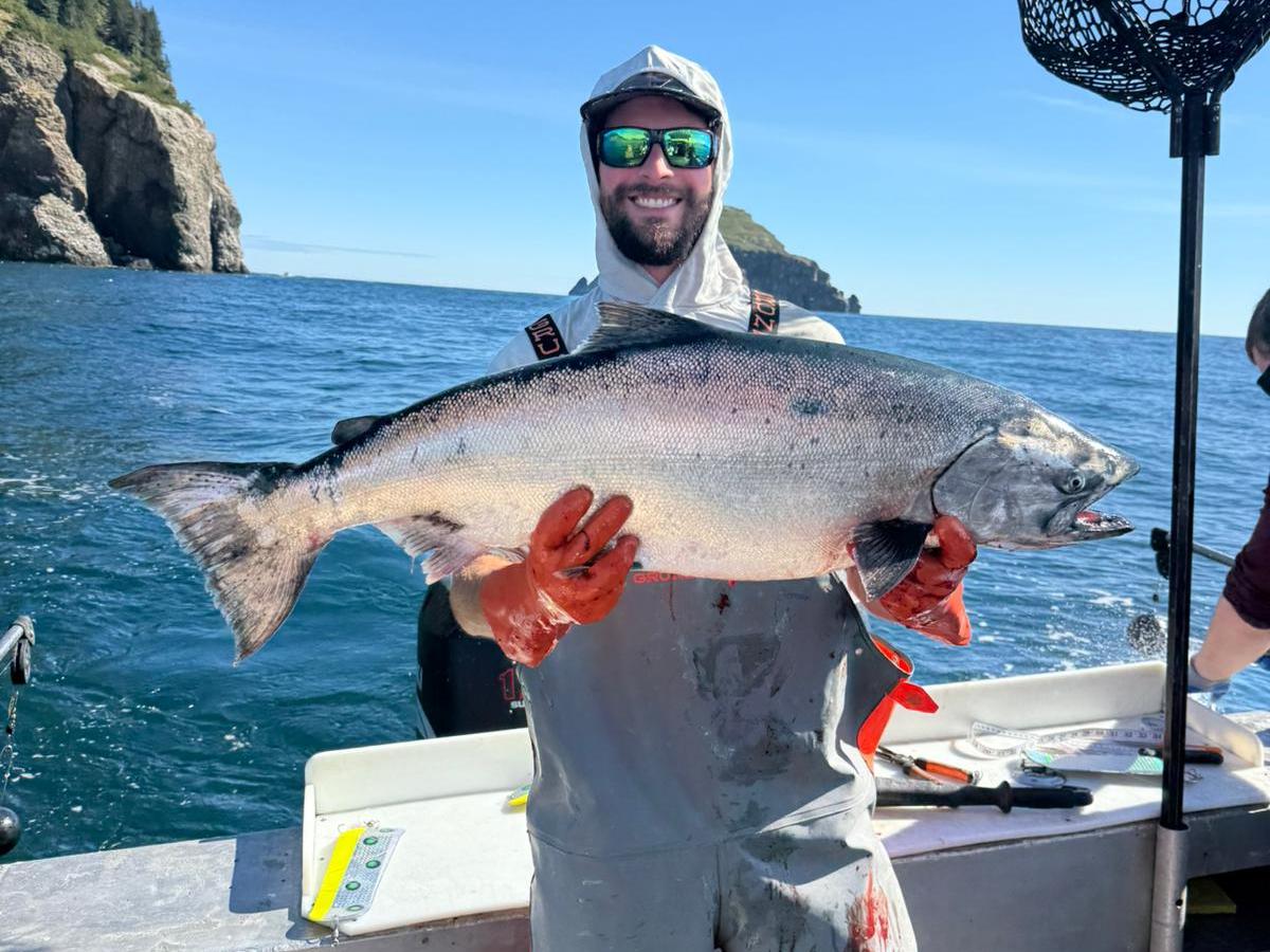 Person holding large fish on boat with ocean and cliffs in the background.