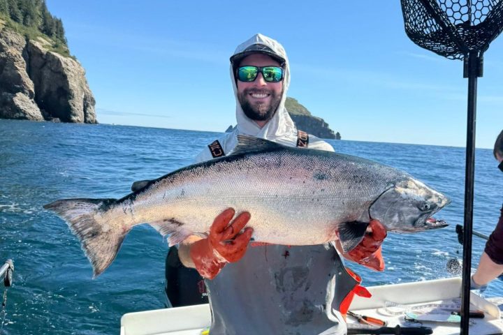 Person on a boat holding a large fish, with ocean and rocky cliffs in the background.