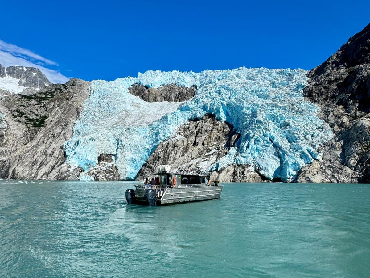 A boat on turquoise water with a glacier and rocky mountains under a clear blue sky.
