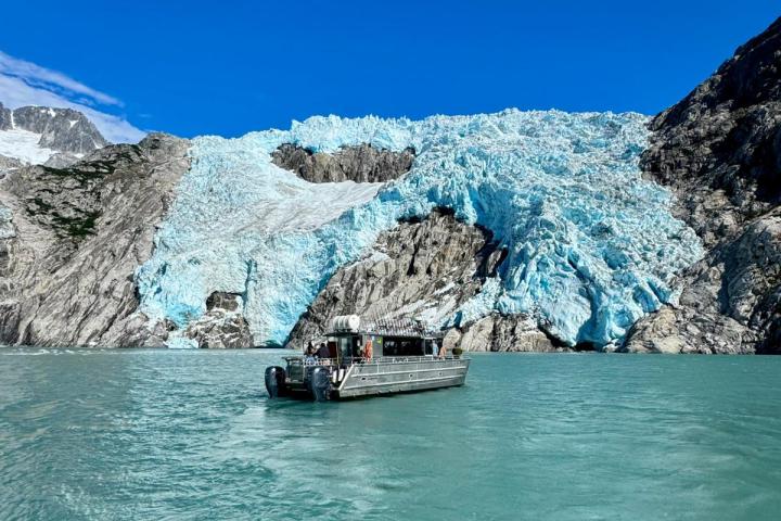 A boat on turquoise water with a glacier and rocky mountains under a clear blue sky.