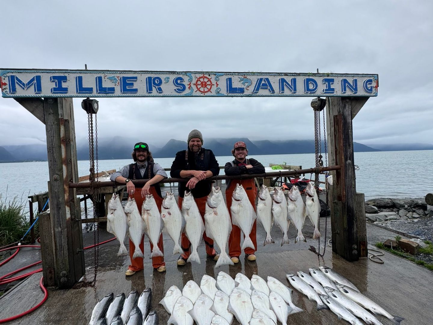 Three people at Miller's Landing display large halibut and other fish on a dock.