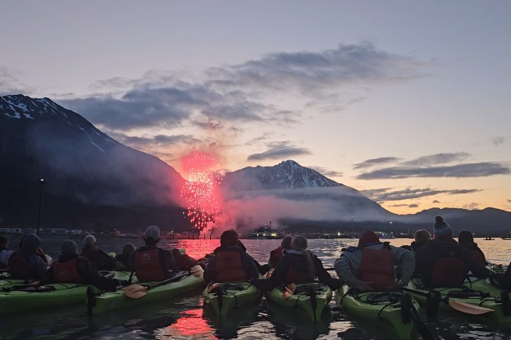 People in kayaks watching fireworks over a mountain at sunset.