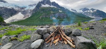 Campfire by a lake with snowy mountains in the background.