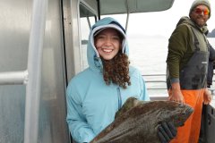 Two people on a boat, one holding a large fish, both in outdoor gear.