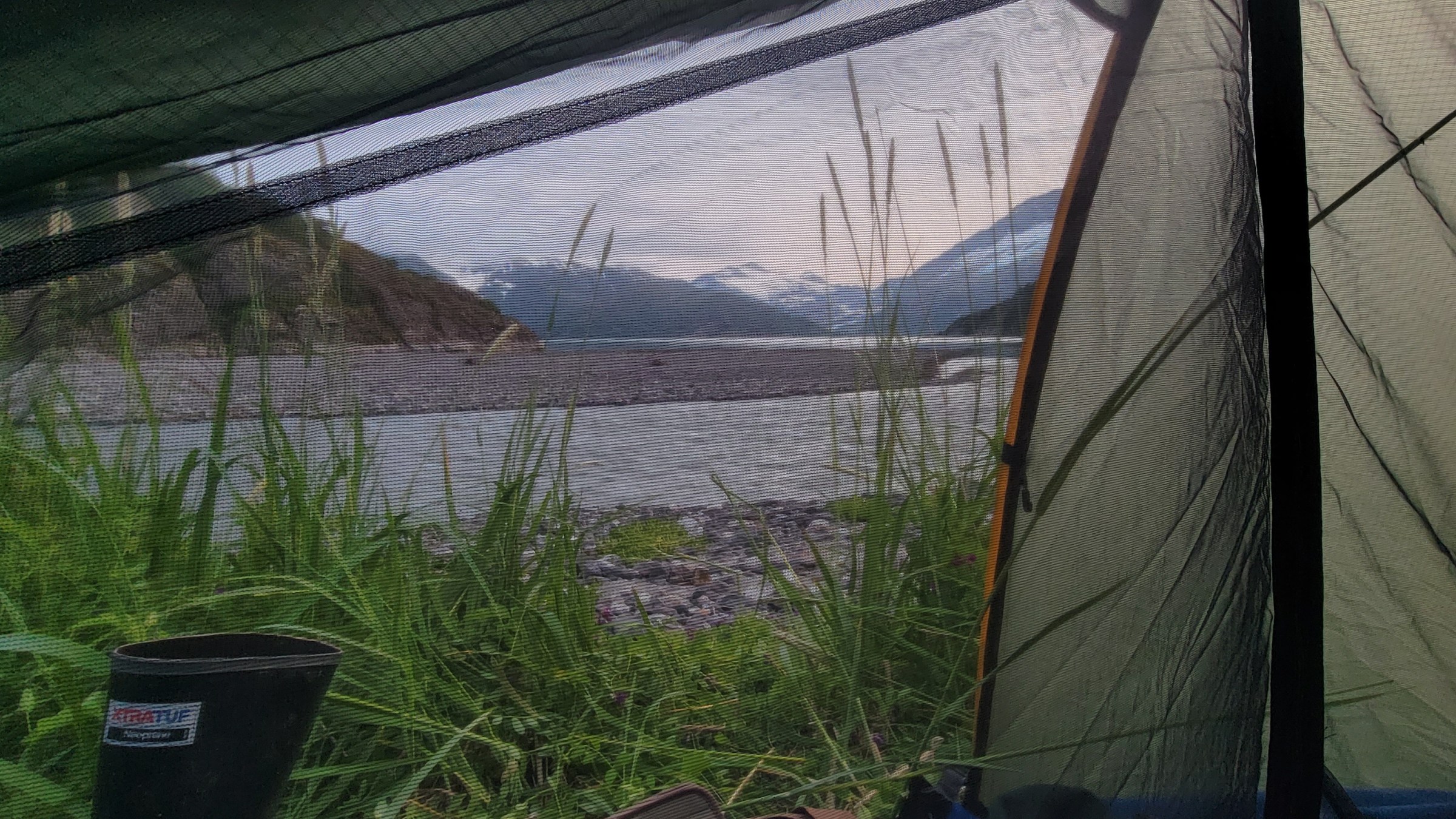 View from a tent of a riverside with mountains in the background.