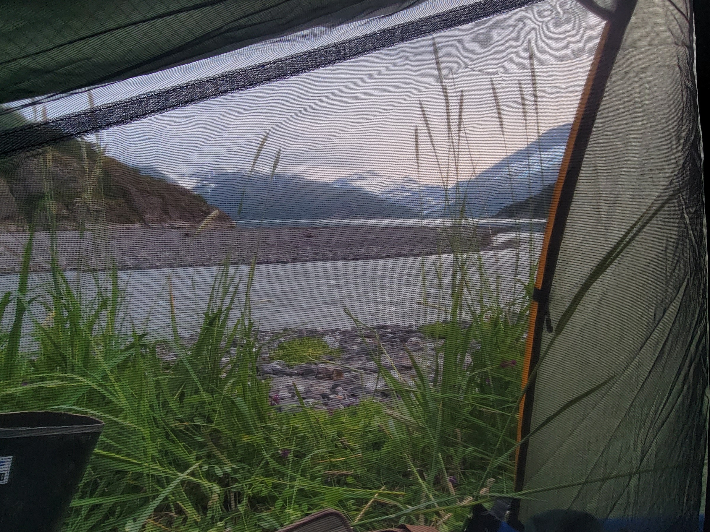 View from a tent of a riverside with mountains in the background.