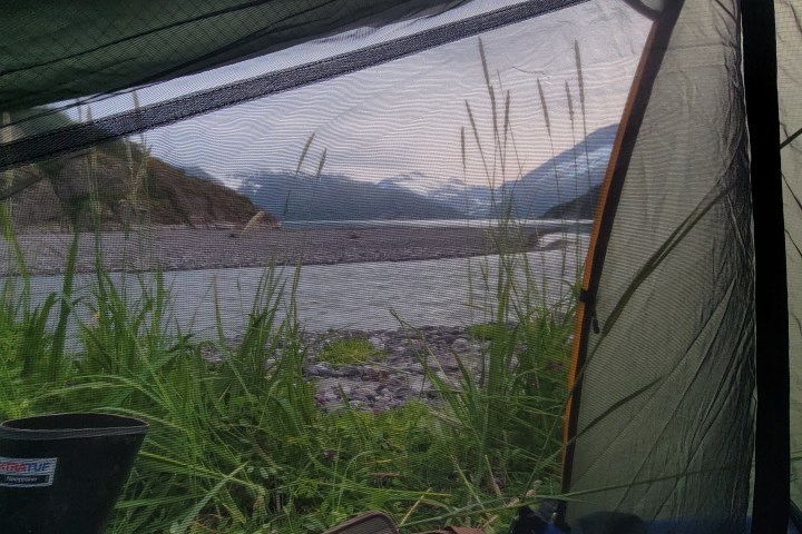 View from a tent of a riverside with mountains in the background.