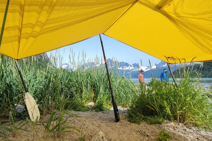View of mountains and lake under a yellow tent with grass in the foreground.