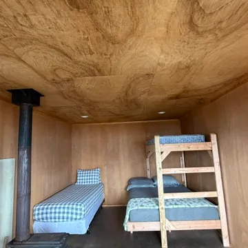 Wooden room with bunk bed, single bed, and wood stove.