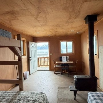Cozy wooden room with bunk bed, stove, and table, mountain view through window.