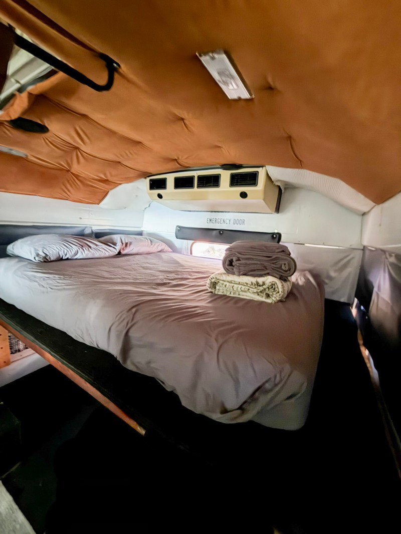 Cozy van interior with a bed, pillows, and folded blankets on a raised platform.