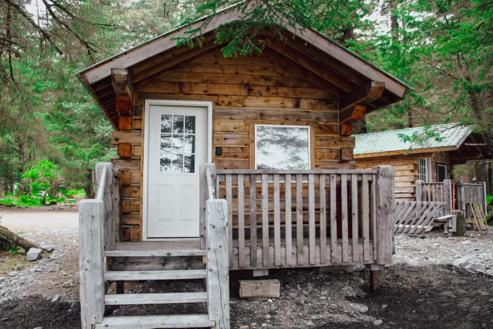 Wooden cabin with a front porch nestled in a forested area.