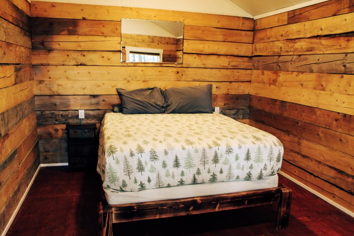 Rustic bedroom with wood walls, patterned bedspread, and a mirror above the bed.