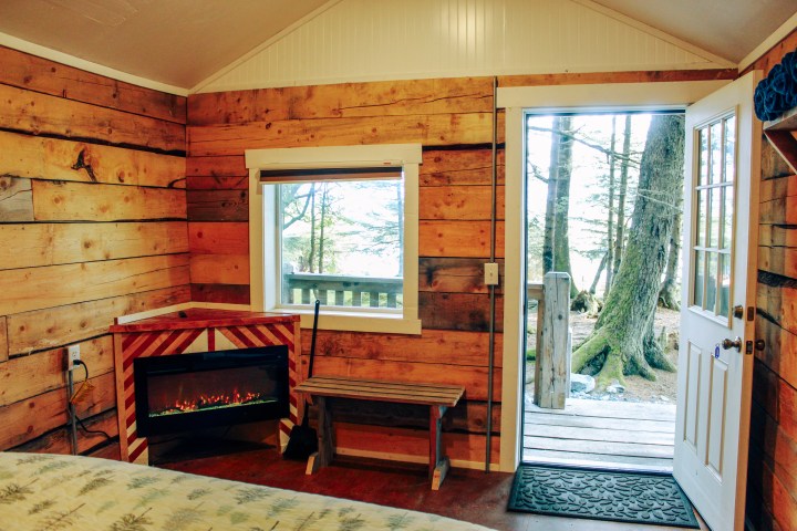 Cozy cabin interior with fireplace, window, and open door to forest scene.