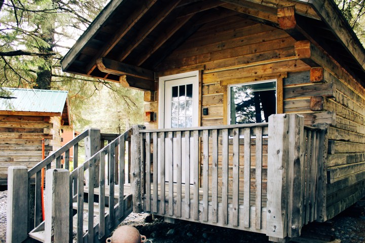 Rustic wooden cabin with a porch and surrounding trees.
